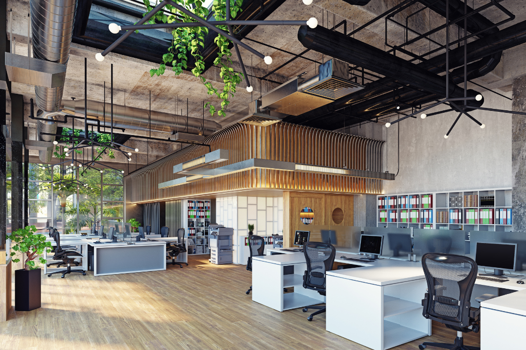 Modern open-plan office with rows of desks, ergonomic chairs, desktop computers, bookshelves, large windows, indoor plants, wooden floors, and industrial-style ceiling with exposed pipes and light fixtures.